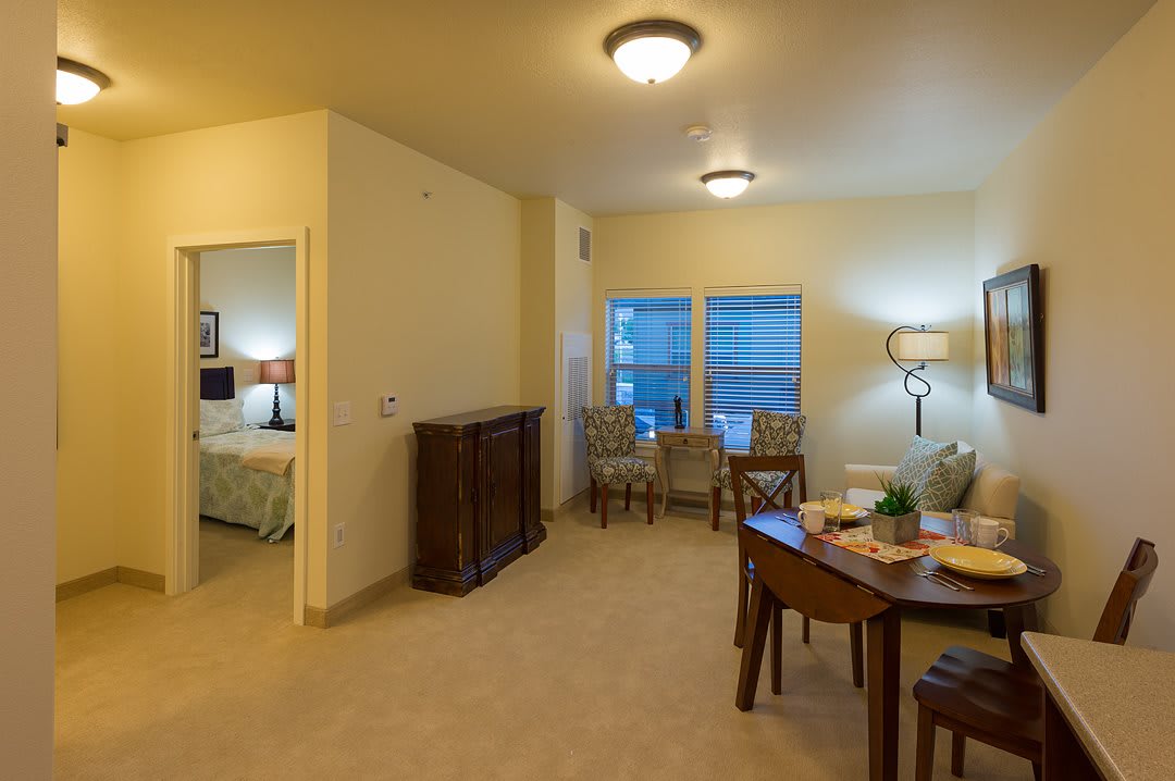 A cozy living room and dining area with adjoining bedroom, featuring stylish furniture and ample lighting.