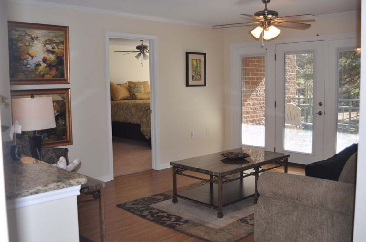 A cozy living room with a coffee table and ceiling fan, leading to a bedroom through an open doorway.