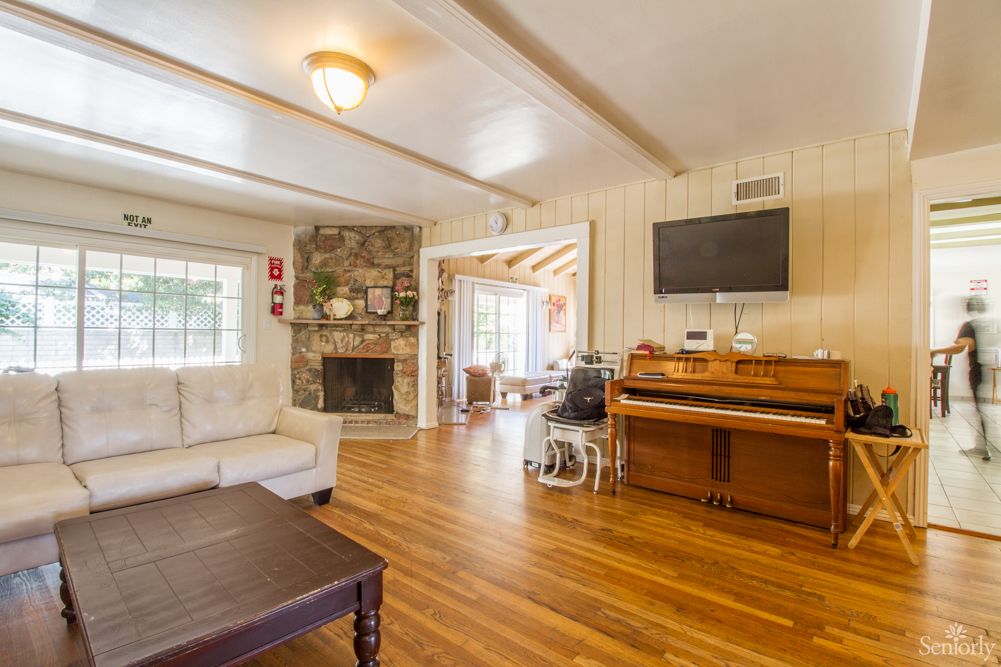 A cozy living room with a piano, stone fireplace, and hardwood floors.