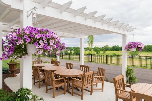 A cozy outdoor patio with wooden furniture under a pergola, adorned with hanging flowers and overlooking a scenic landscape.