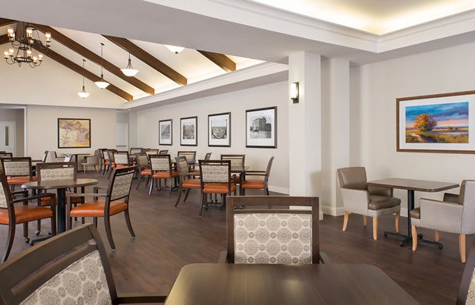A modern dining room with neatly arranged tables and chairs, decorated with framed pictures and wooden ceiling beams.