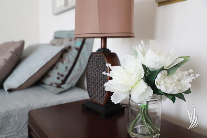 A cozy bedside setup featuring a decorative lamp and a vase of white flowers.