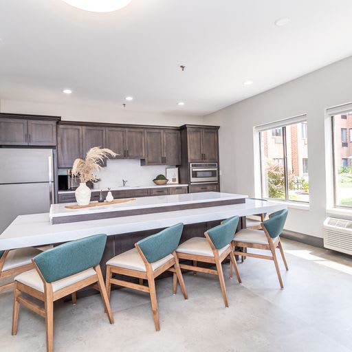 A modern kitchen with a large island and stylish seating, illuminated by natural light through the windows.