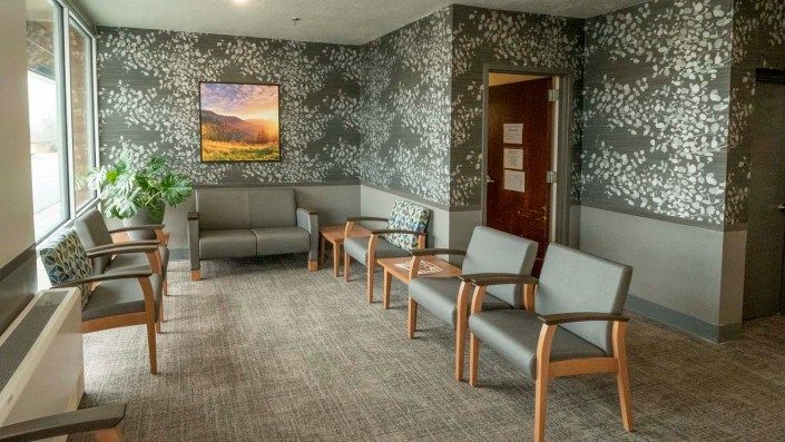 A calm and neatly arranged waiting room with multiple chairs, a painting on the wall, and patterned wallpaper.