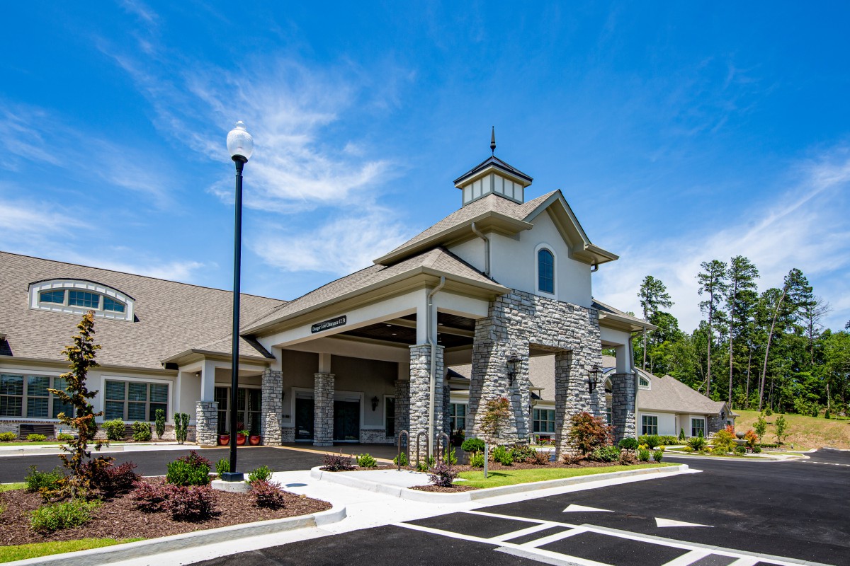 A modern building with a stone facade and landscaped entrance under a clear blue sky.