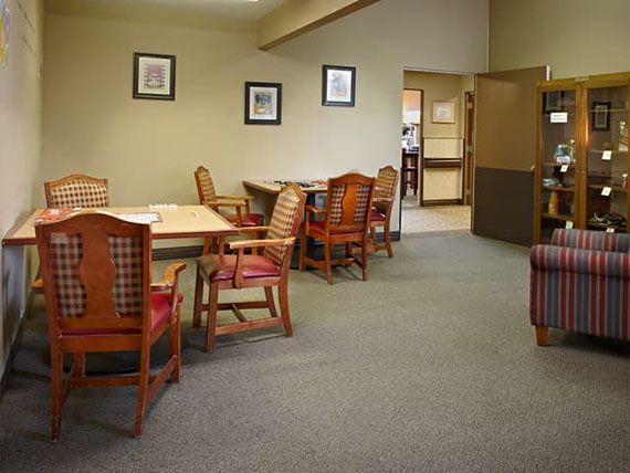 A cozy dining area with wooden chairs and tables, set against a carpeted floor and decorated with framed art on the walls.