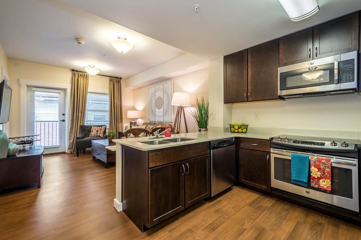 A modern open concept kitchen and living area with wood flooring and stainless steel appliances.