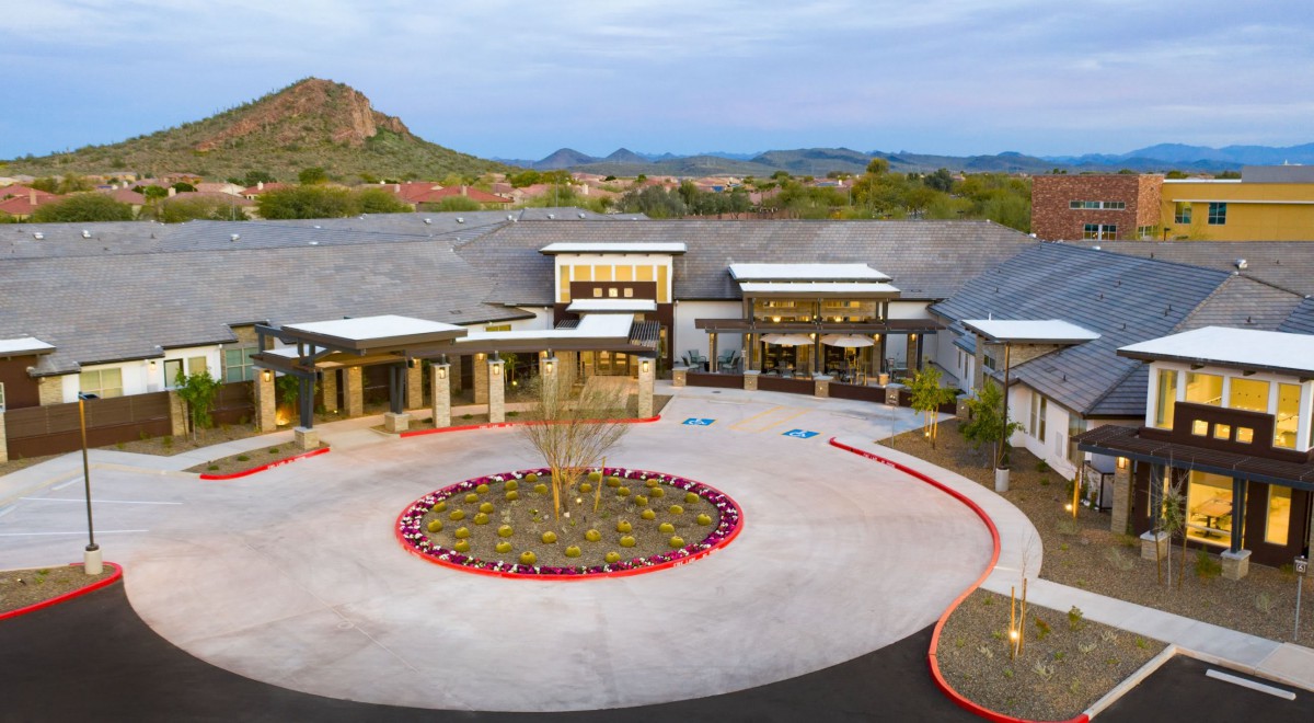 A modern building entrance with a circular fountain, set against a desert landscape backdrop.