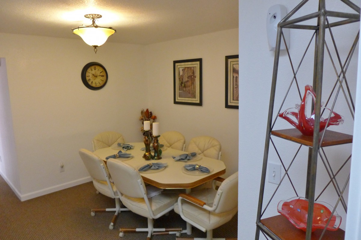 A cozy dining room featuring a set of six chairs around a wooden table, decorated with placemats and candles, complemented by wall art and a clock.