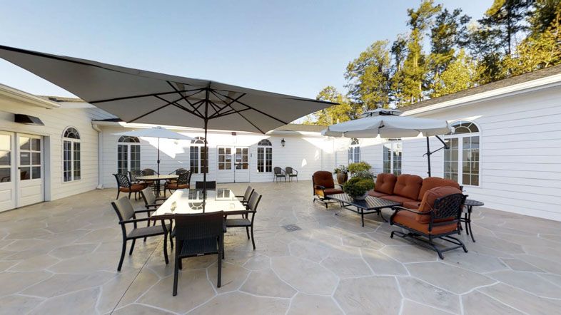 A spacious patio with outdoor furniture including tables, chairs, and large umbrellas on a sunny day.