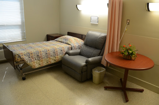 A serene hospital room featuring a bed, a recliner chair, and a small table with flowers.