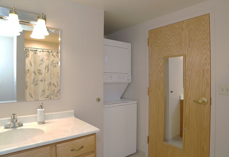 A bathroom with a mirror, sink, and a stacked washer and dryer unit.