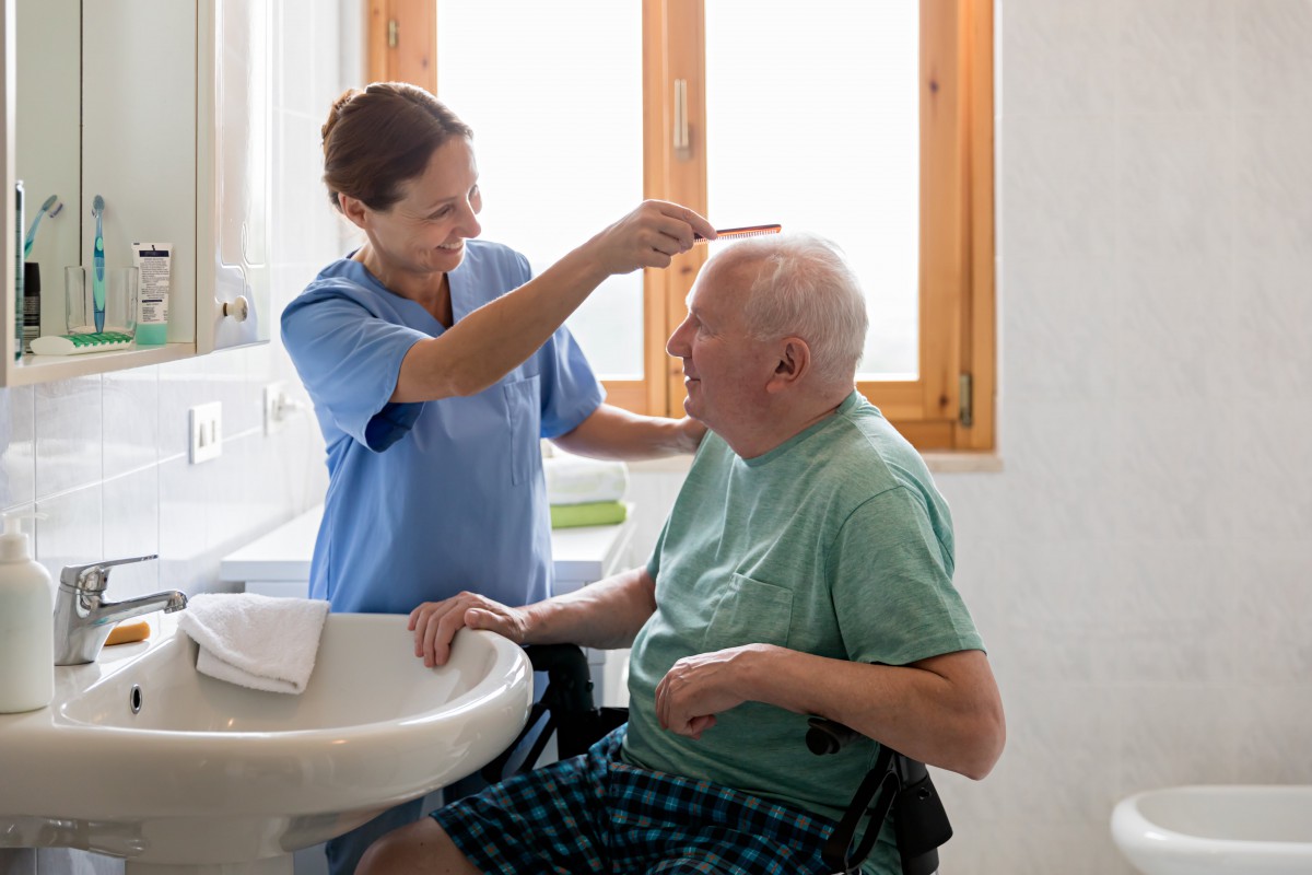 A caregiver assists an elderly man by combing his hair in a home setting.