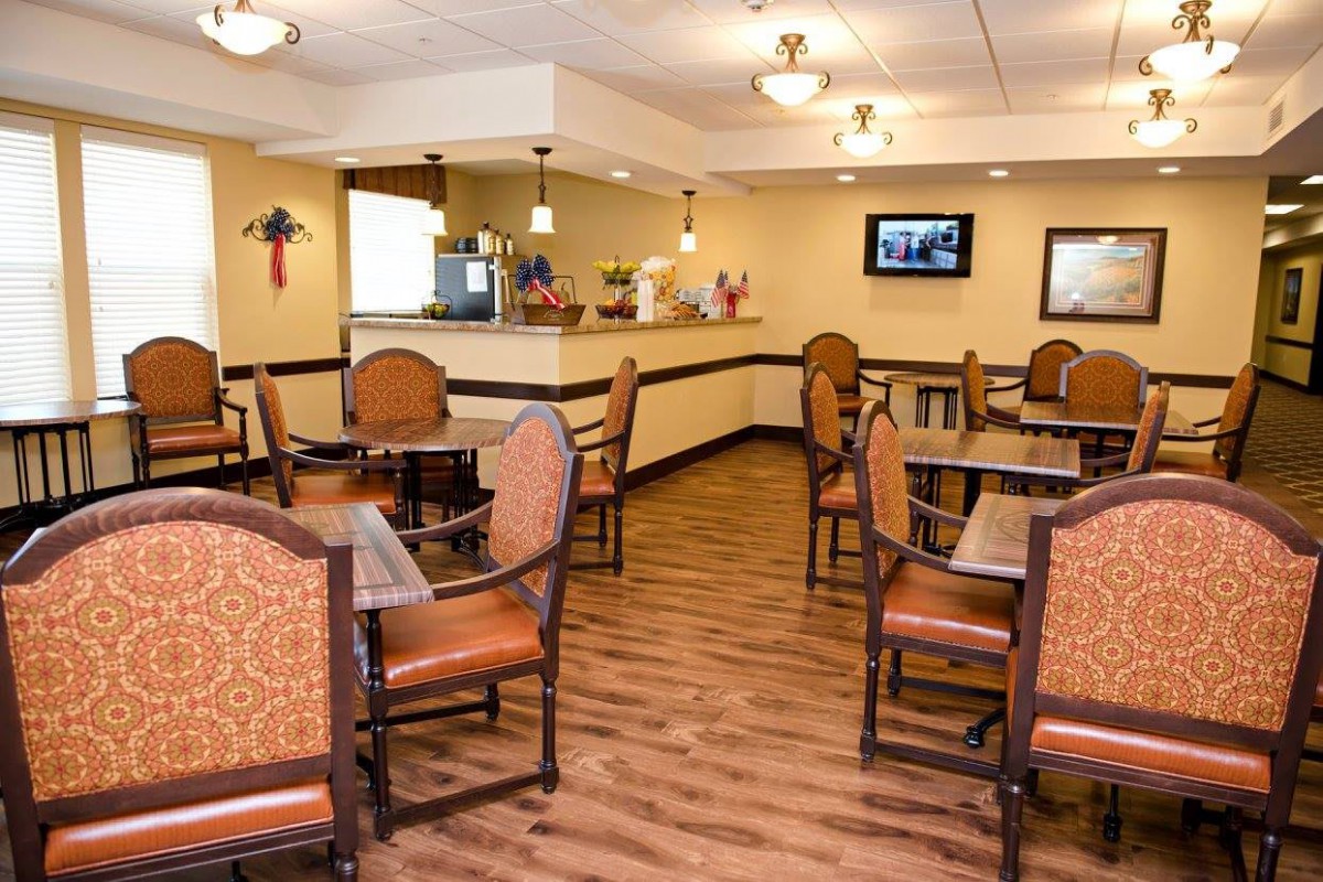 A cozy dining area featuring several tables and chairs, with warm lighting and a television on the wall.
