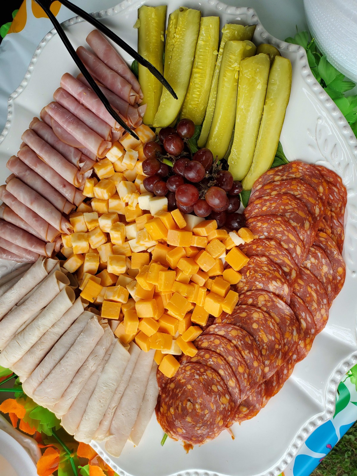A charcuterie platter featuring sliced meats, assorted cheeses, grapes, and pickles.