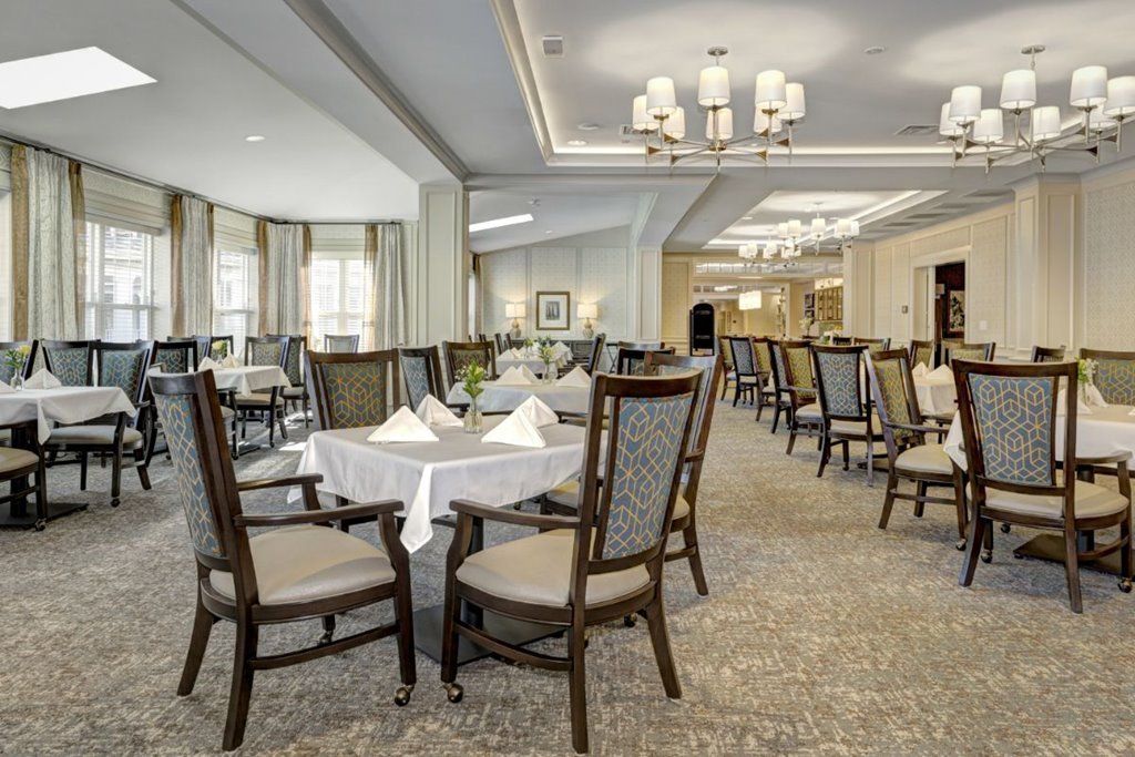 An elegant dining room with neatly arranged tables and chairs, illuminated by chandeliers.