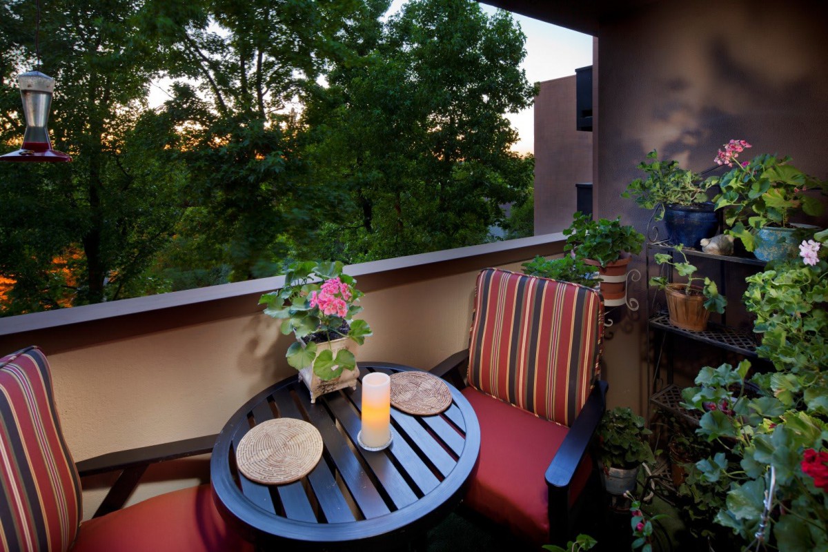 A cozy balcony setup with a small table and chairs, surrounded by lush greenery in the evening light.