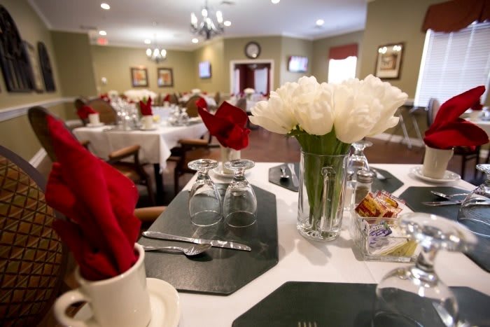 A beautifully set dining table in a restaurant, featuring red napkins and a bouquet of white flowers.