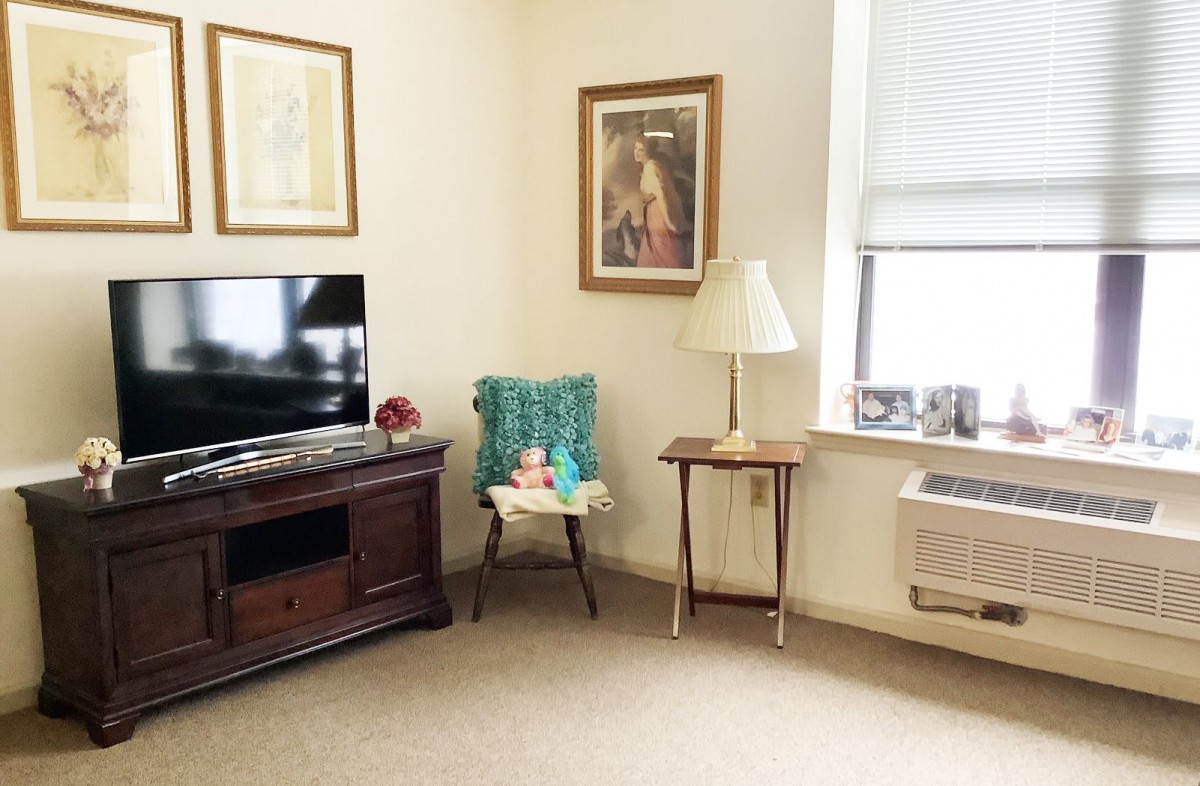 A cozy living room with a television, chair, and lamp, featuring artwork on the walls.