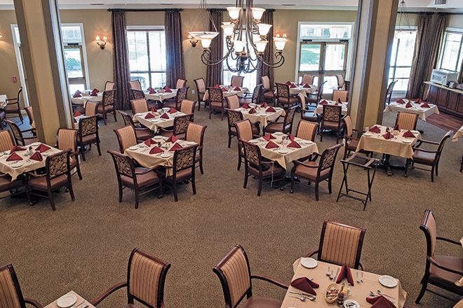 A spacious dining room with neatly arranged tables and chairs, featuring elegant chandeliers and large windows.