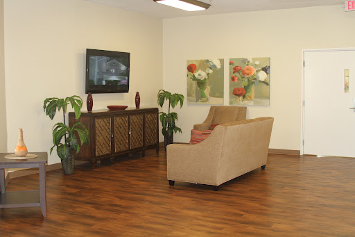 A cozy living room setting featuring a beige sofa, a TV, decorative plants, and vibrant artwork on the walls.