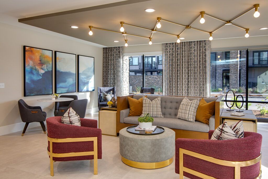 A modern living room with stylish furniture, including a grey tufted sofa, red armchairs, and a round coffee table, accented by decorative pillows and contemporary lighting.