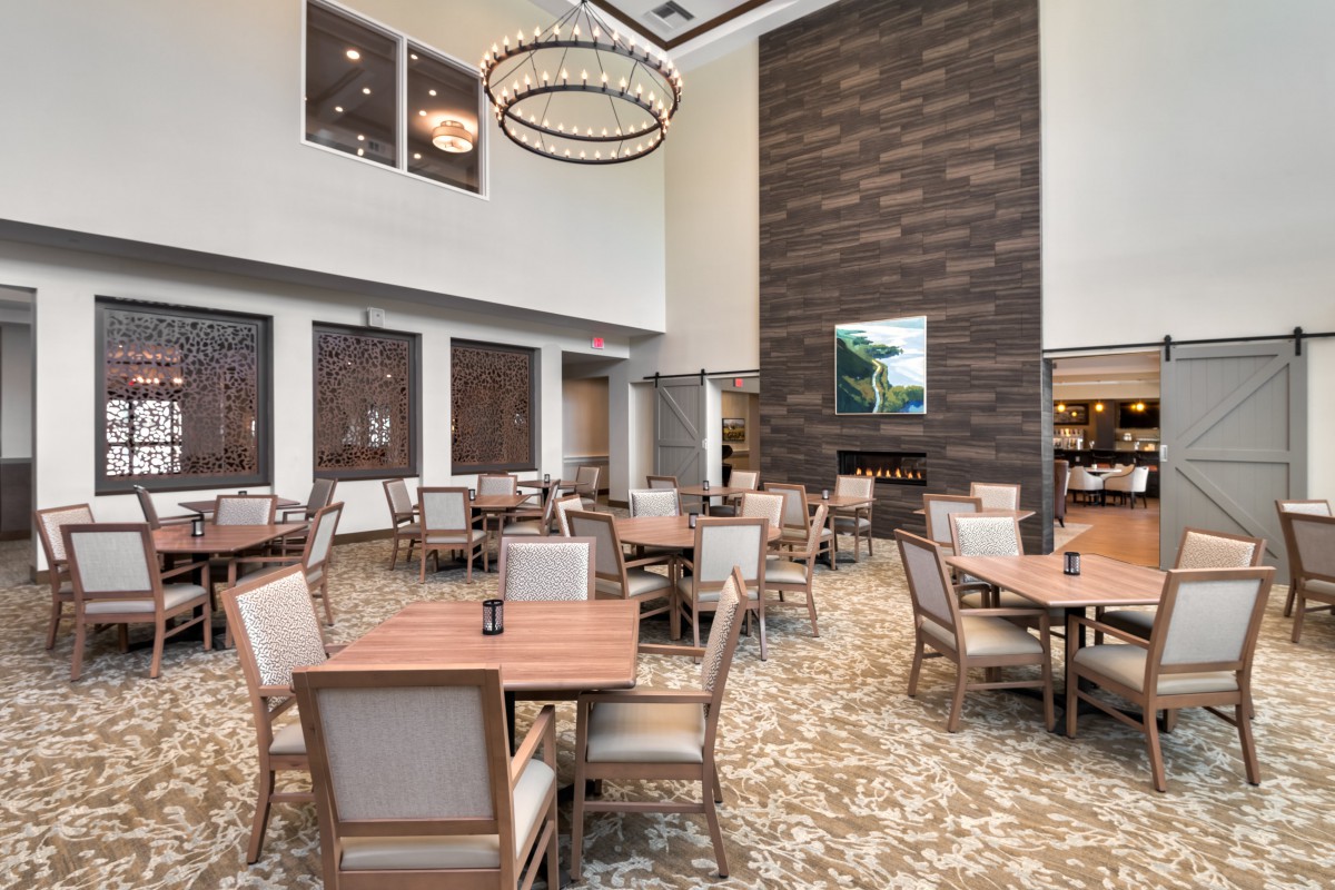 A spacious and modern dining area with neatly arranged tables and chairs under a large chandelier.