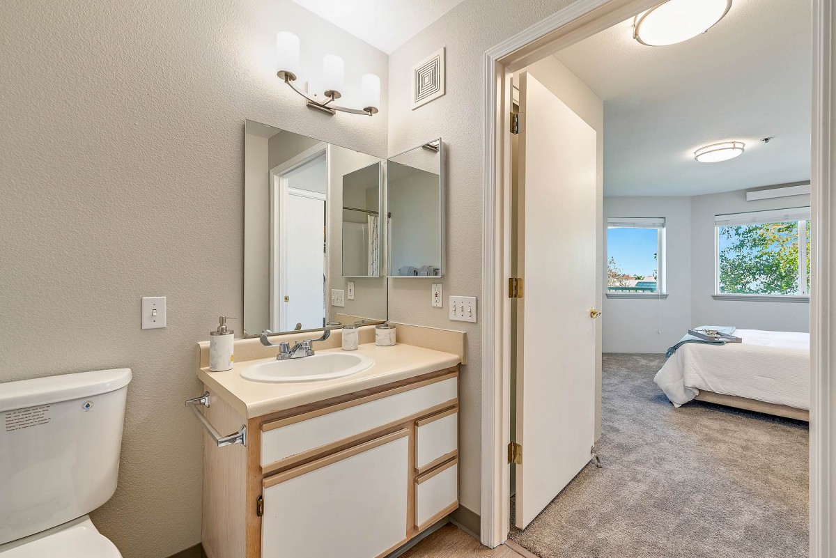 A modern bathroom featuring a sink with a mirror and cabinet, leading into a bedroom.