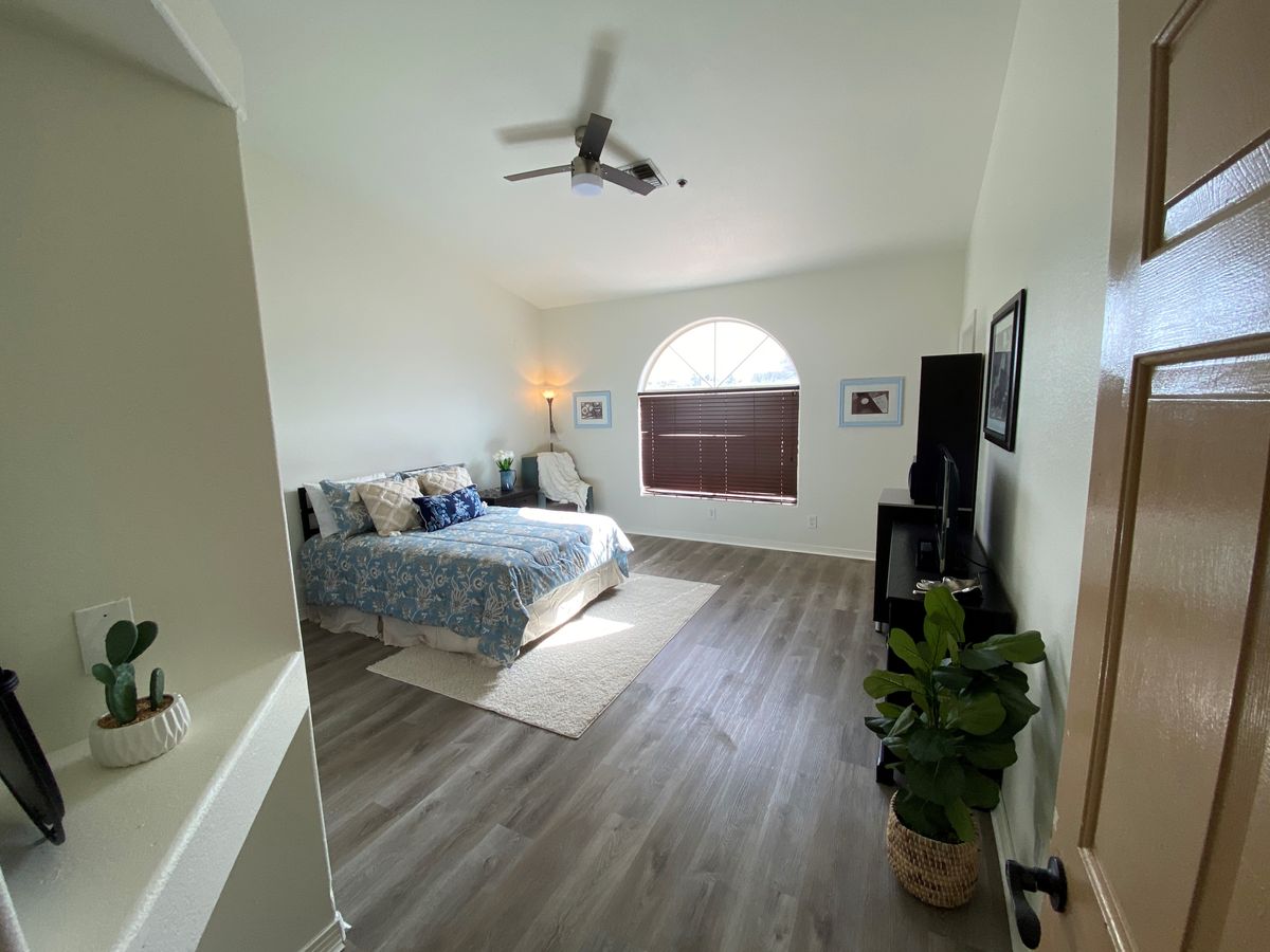 A spacious, minimalist bedroom with modern decor, featuring a large bed, hardwood flooring, and ample natural light.