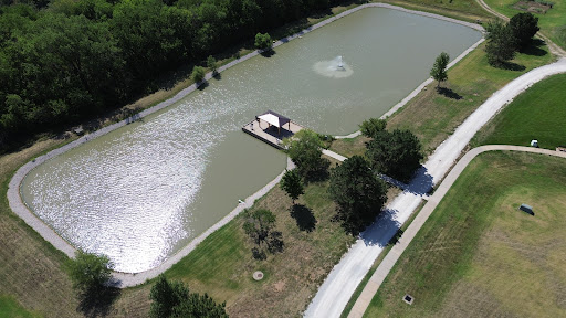A serene aerial view of a pond with a dock and fountain, surrounded by lush greenery.