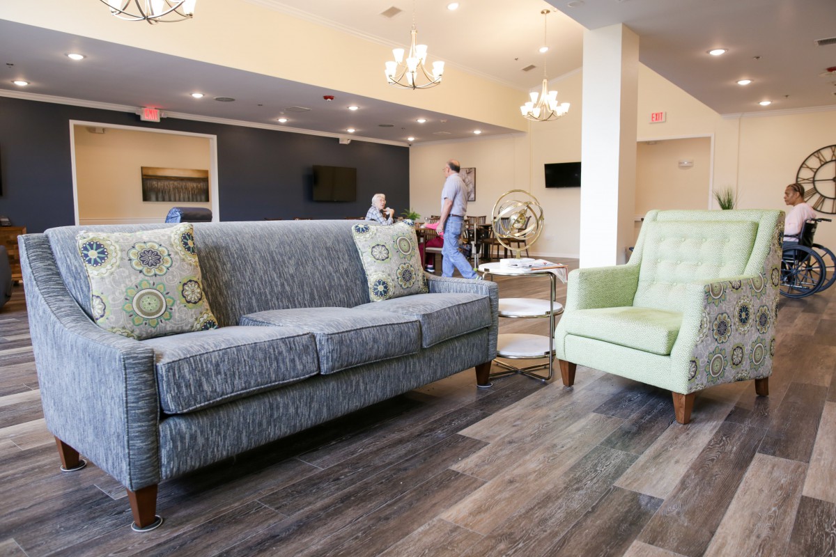 A modern lobby featuring a gray sofa and a green armchair, with elegant chandeliers and wooden flooring.