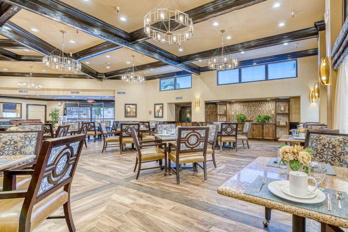 A spacious and modern dining area with elegantly arranged tables and chairs, featuring warm lighting and a wooden floor.