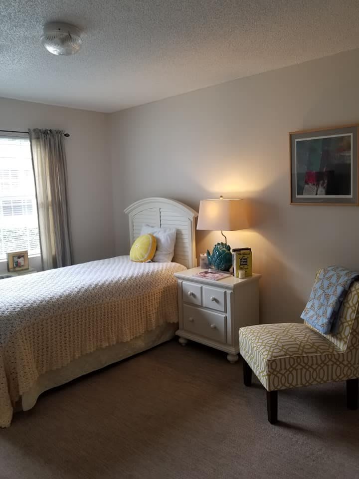 A cozy bedroom with a bed, lamp, and chair near a window.