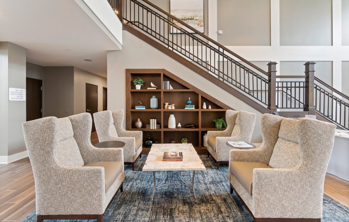 A modern lobby area with comfortable armchairs, a central table, and a stylish bookshelf under a staircase.