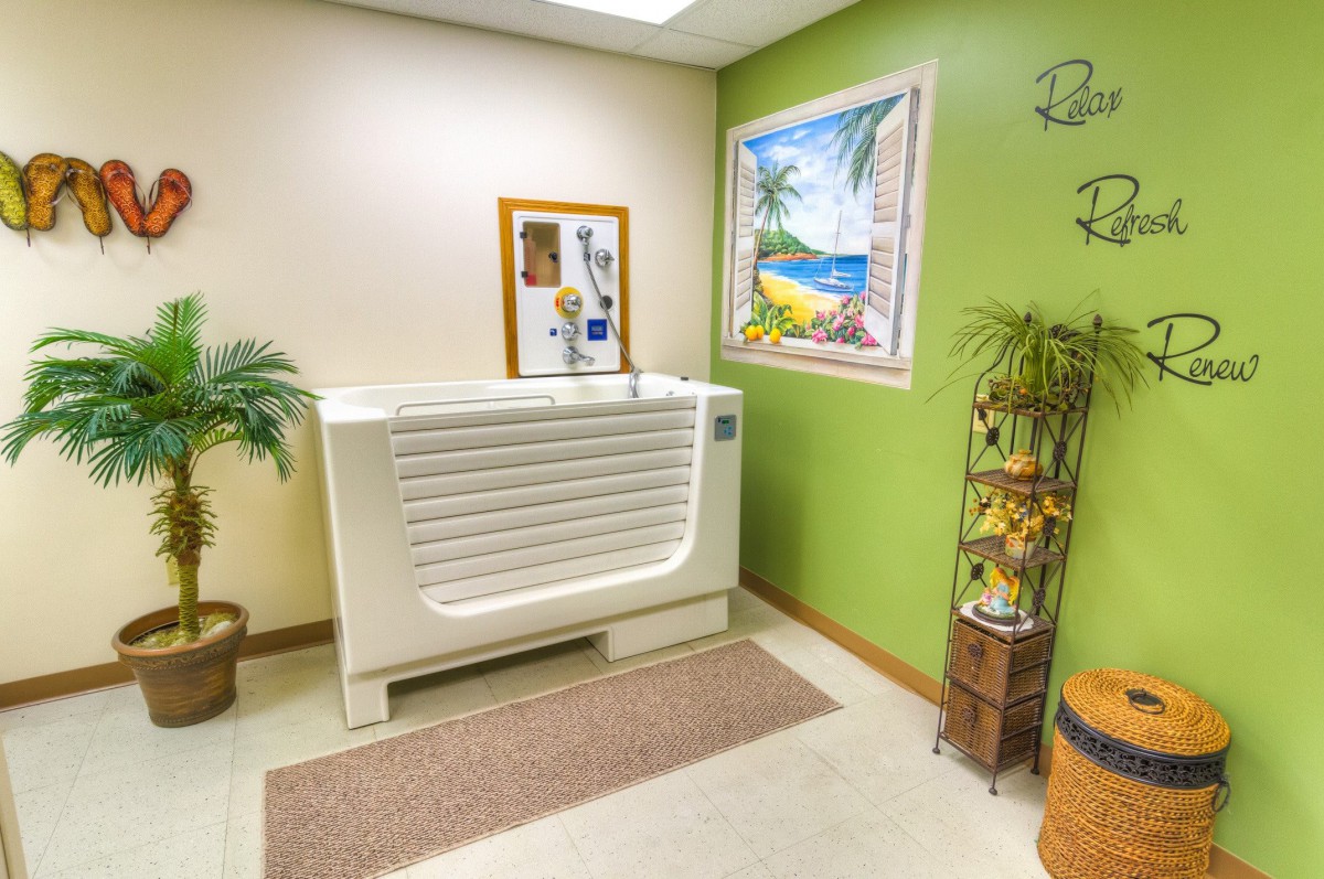 A bathroom interior featuring a bathtub, artwork, and decorative plants against a green wall.