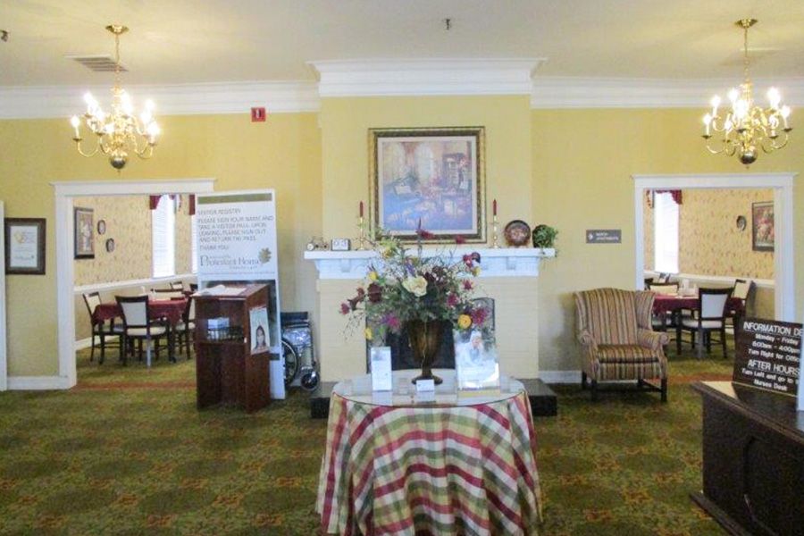 A cozy lobby area featuring a round table with a floral centerpiece, a painting above a fireplace, and comfortable seating.