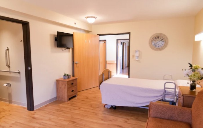A clean and organized hospital room with wooden flooring, featuring a bed, television, and essential furniture.