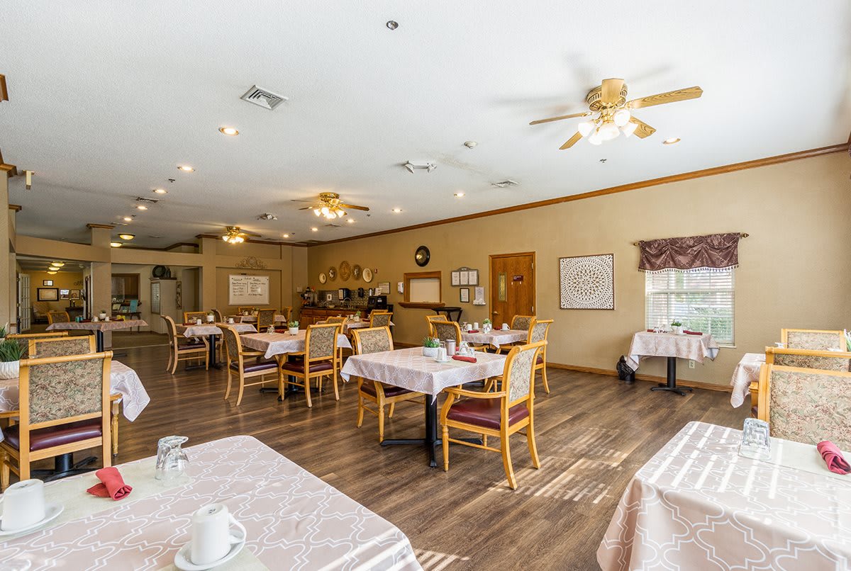 A spacious dining room with neatly arranged tables and chairs, featuring wood flooring and ceiling fans.
