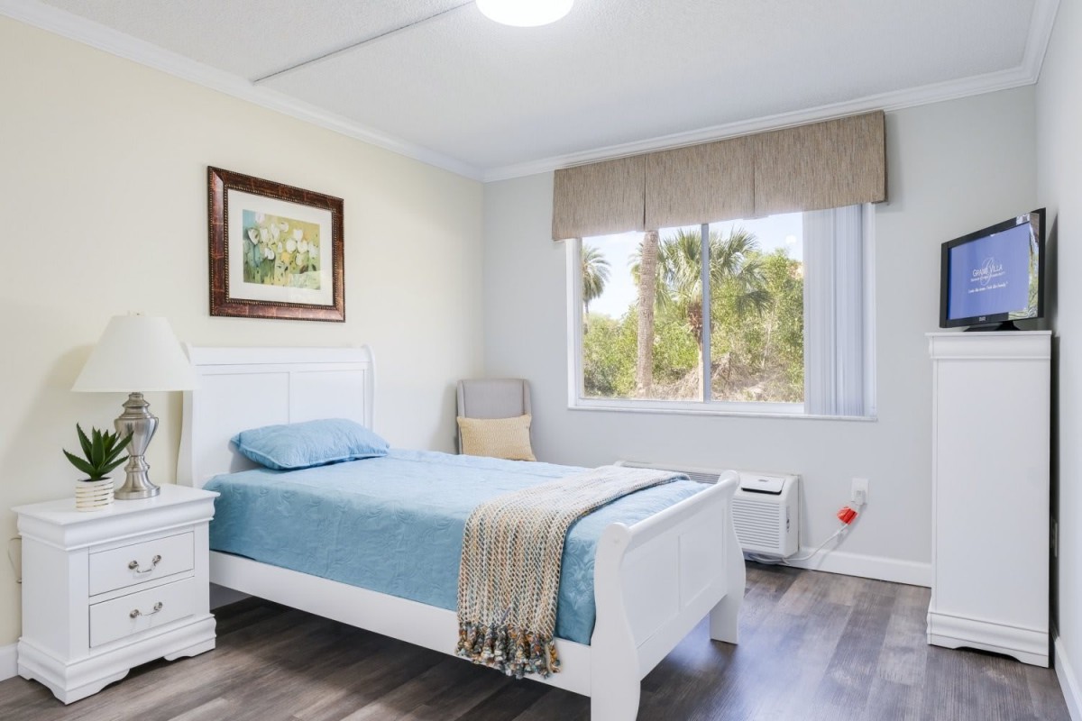 A bright and minimalist bedroom featuring a single bed with blue bedding, a window allowing natural light, and simple decor.