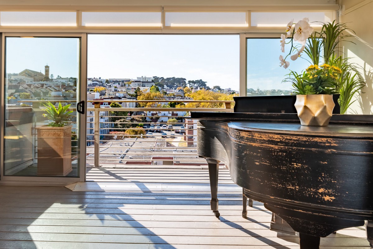 A grand piano in a bright living room with a view of the city through large windows.
