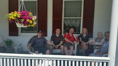 A group of people sitting on a porch with hanging flowers nearby.