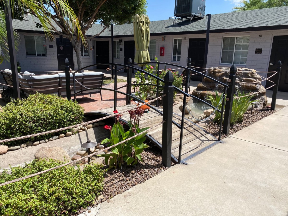 A serene courtyard with a pathway leading to benches, surrounded by plants and enclosed by a fence.