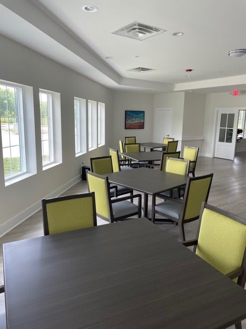 A bright and airy dining area with multiple tables and chairs, illuminated by natural light from large windows.