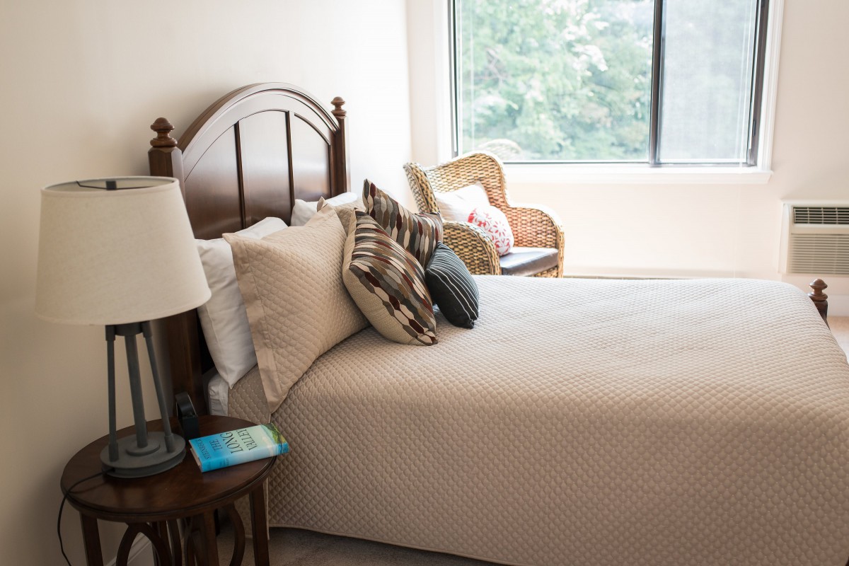 A cozy bedroom with a neatly made bed, decorative pillows, and a large window.