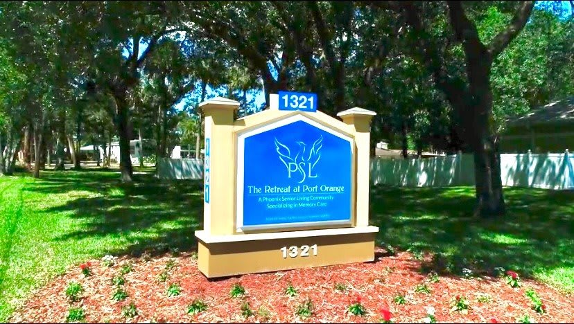 A school sign with the text 'PSL The School at MPI College' displayed in an outdoor setting surrounded by trees and well-maintained landscaping.