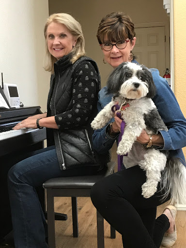 Two women enjoying a moment together at the piano with a dog.