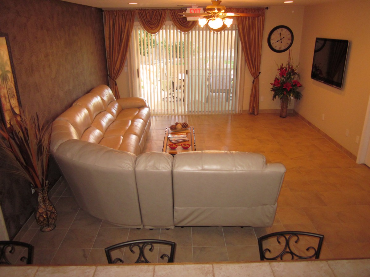 A cozy living room with a large sectional sofa and a coffee table, featuring elegant curtains and a ceiling fan.