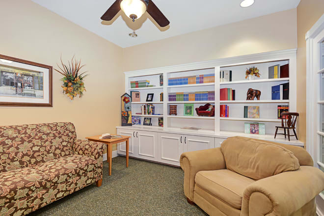 A cozy living room with armchairs, a bookshelf, and a ceiling fan.