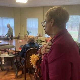 A woman standing in a senior activity room, observing while others are seated.
