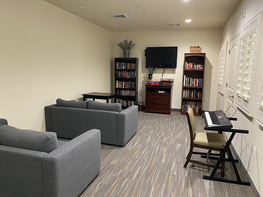 A cozy living room with sofas, bookshelves, a piano, and a television.